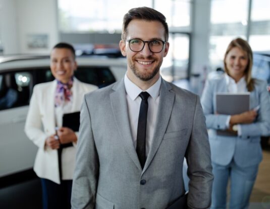 Équipe de gestionnaires souriants en salle de montre, illustrant le leadership en concession automobile.