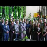 A large group of smiling professionals, business partners, and Unimax management posing for a group photo inside the new high-ceilinged Stox warehouse in Ottawa, with bright green industrial tire racks and inventory visible in the background.